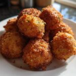 A close-up of several golden brown Air Fryer Crispy Parmesan Broccoli Tots piled on a white plate.