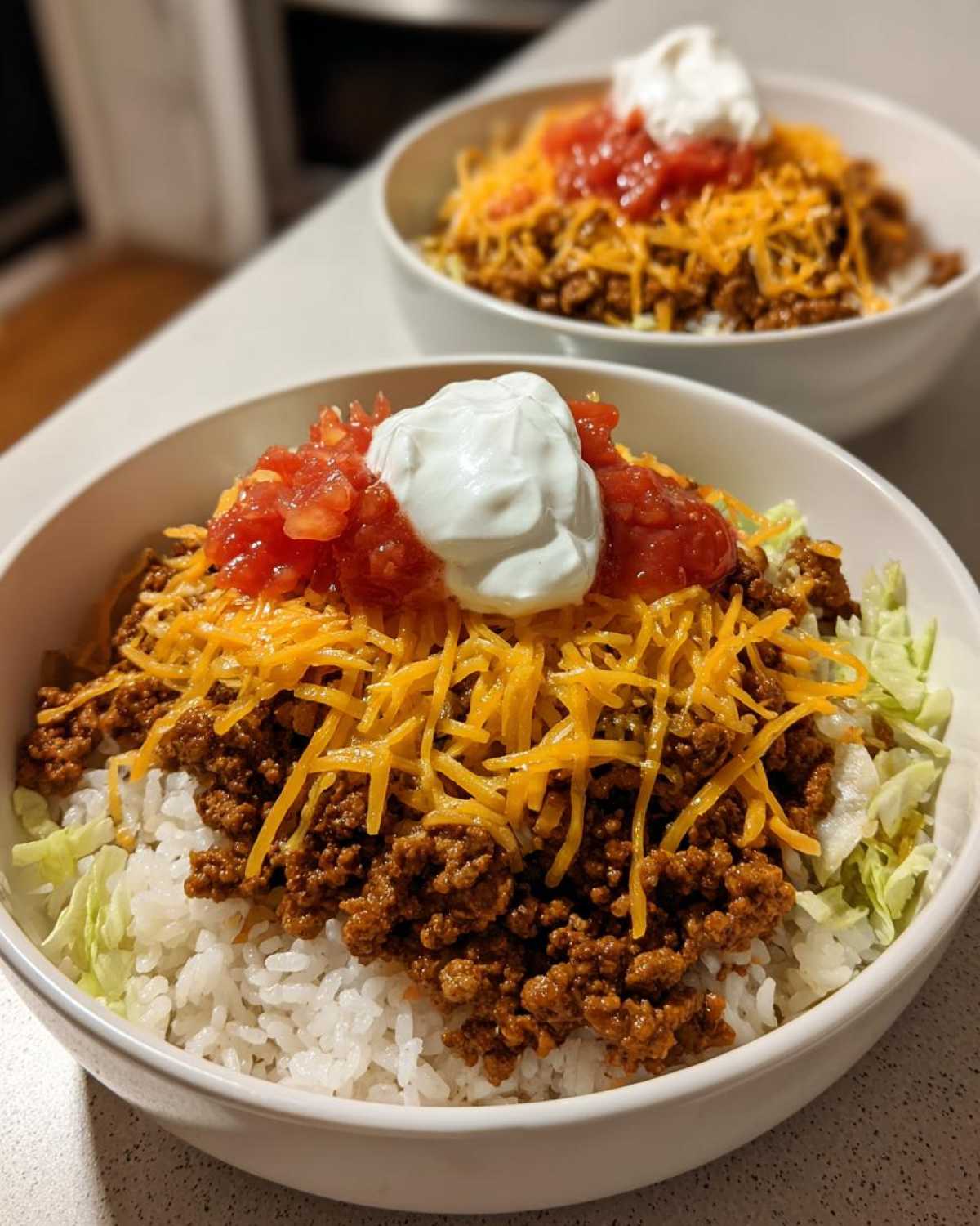 A close-up of an Air Fryer Crispy Turkey Taco Bowl layered with rice, seasoned ground turkey, shredded cheese, salsa, and sour cream.