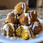 A pile of golden brown Air Fryer Herb Falafel Balls drizzled generously with white tahini sauce.