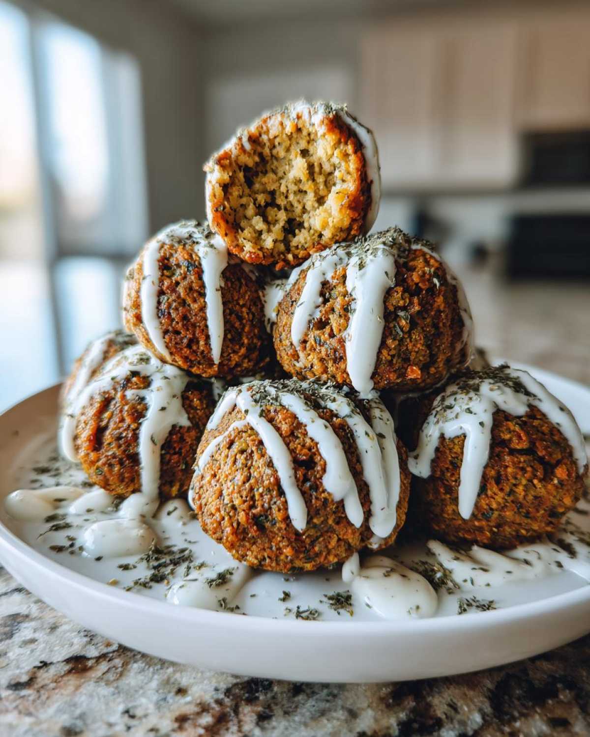 A stack of crispy Air Fryer Herb Falafel Balls drizzled with white tahini sauce and sprinkled with dried herbs.
