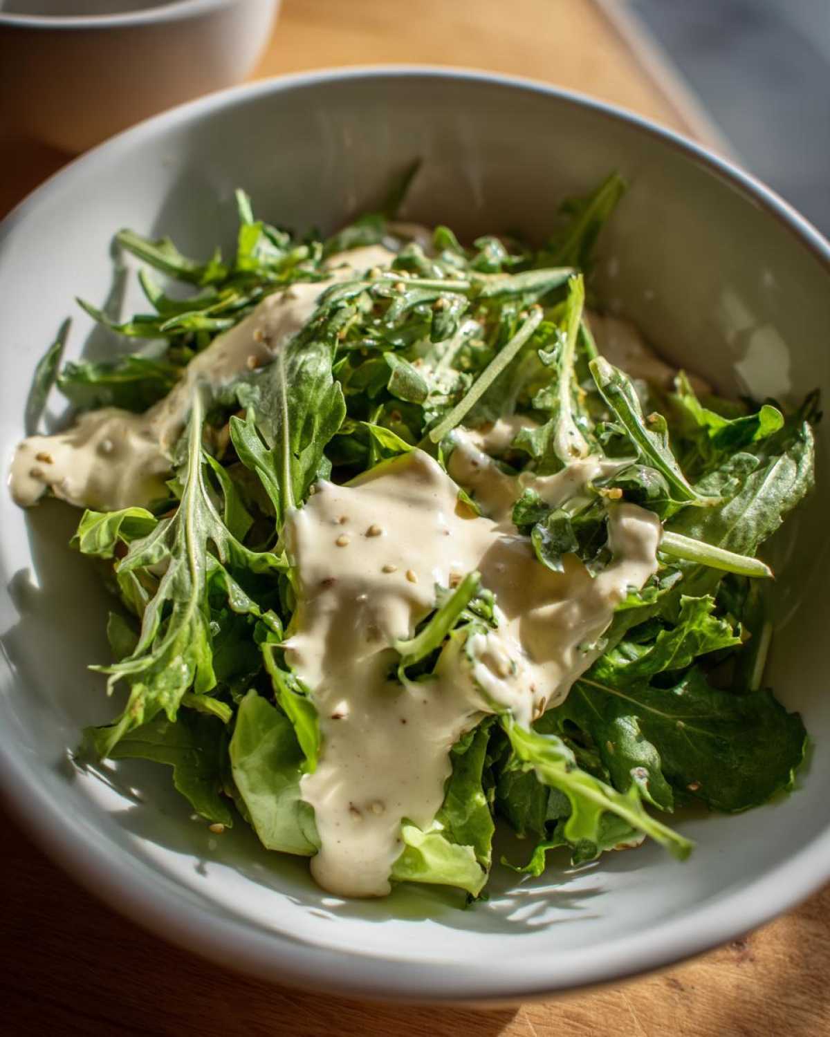 A close-up of fresh arugula salad generously topped with Vegan Creamy Lemon Tahini Dressing in a light bowl.