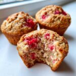 Close-up of a Gluten-Free Strawberry Oat Muffin with a bite taken out, showing moist crumb and bright red strawberries.