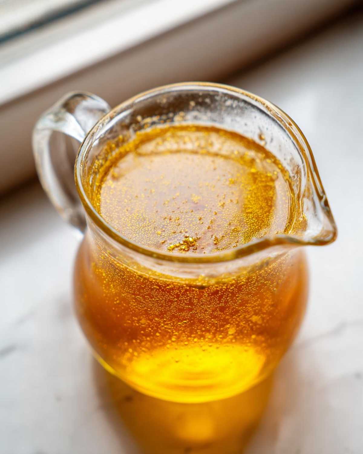 Close-up of bright amber Copycat Apple Cider Vinaigrette with small bubbles in a clear glass pitcher.