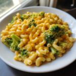 A close-up, appetizing shot of Copycat Café Broccoli Cheddar Mac, featuring elbow macaroni coated in rich cheese sauce with bright green broccoli florets.