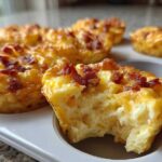 Close-up of Copycat Café-Style Bacon Gruyere Egg Bites in a white muffin tin, one bite has a piece taken out.
