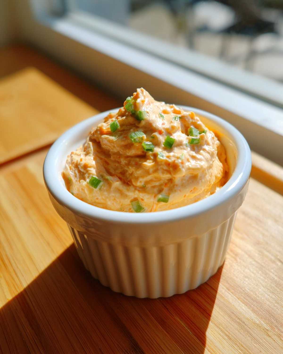 A small white ramekin filled high with creamy orange Copycat Classic Burger Spread Sauce, garnished with chopped green onions.