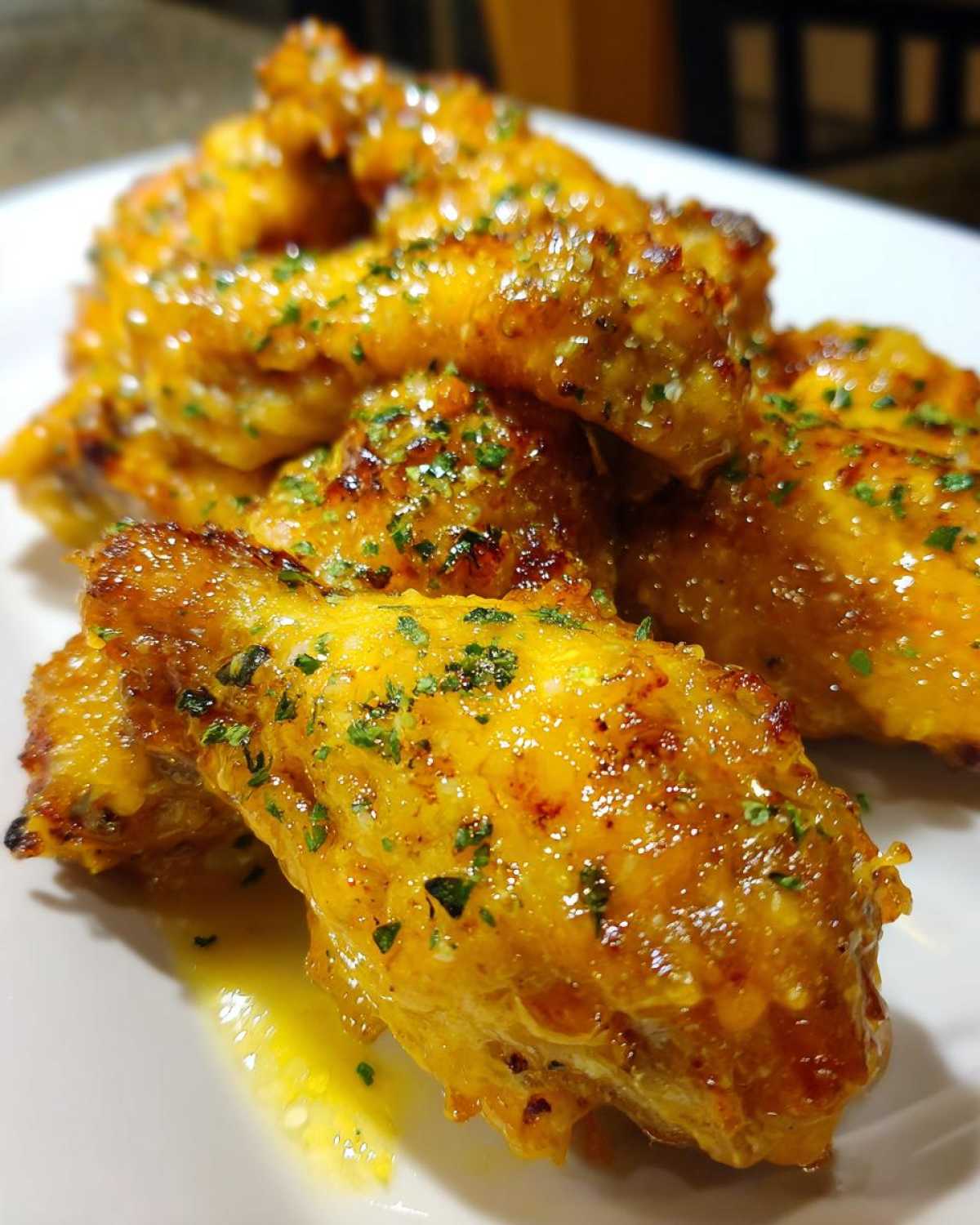 Close-up of crispy chicken wings generously coated in glistening Copycat Garlic Parmesan Wing Sauce and sprinkled with parsley.