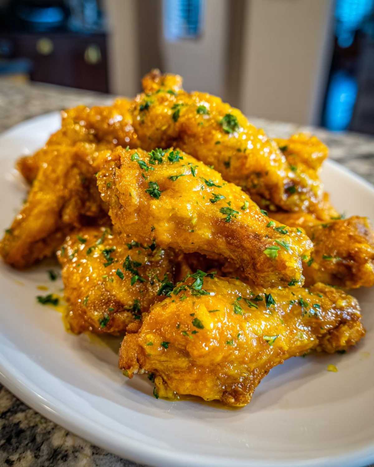A pile of crispy chicken wings generously coated in a glossy, golden Copycat Garlic Parmesan Wing Sauce and sprinkled with fresh parsley.