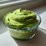 A close-up of thick, vibrant green Copycat Green Goddess Ranch Dressing swirled high in a small, clear glass bowl.
