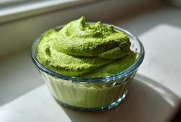 A close-up of thick, vibrant green Copycat Green Goddess Ranch Dressing swirled high in a small, clear glass bowl.