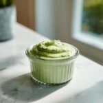 A small glass ramekin filled with thick, vibrant green Copycat Green Goddess Ranch Dressing sitting on a white marble counter.