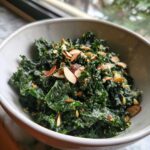 A bowl of Copycat Kale Crunch Salad coated in creamy dressing and topped with sliced almonds and pumpkin seeds.