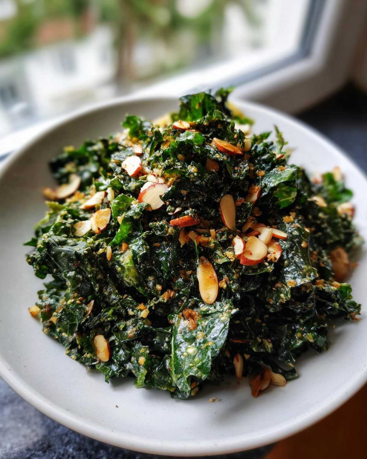 A bowl overflowing with Copycat Kale Crunch Salad, tossed in dressing and topped with sliced almonds.