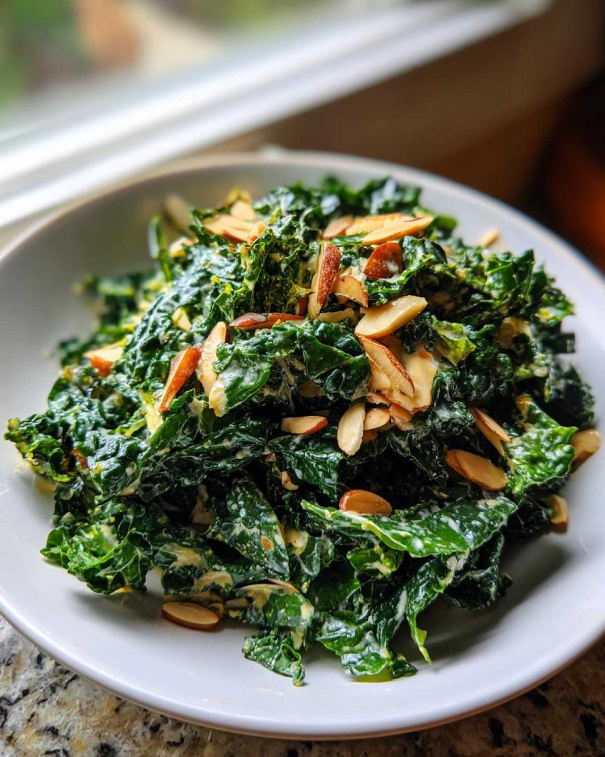 A vibrant bowl of Copycat Kale Crunch Salad tossed in creamy dressing and topped with toasted sliced almonds.