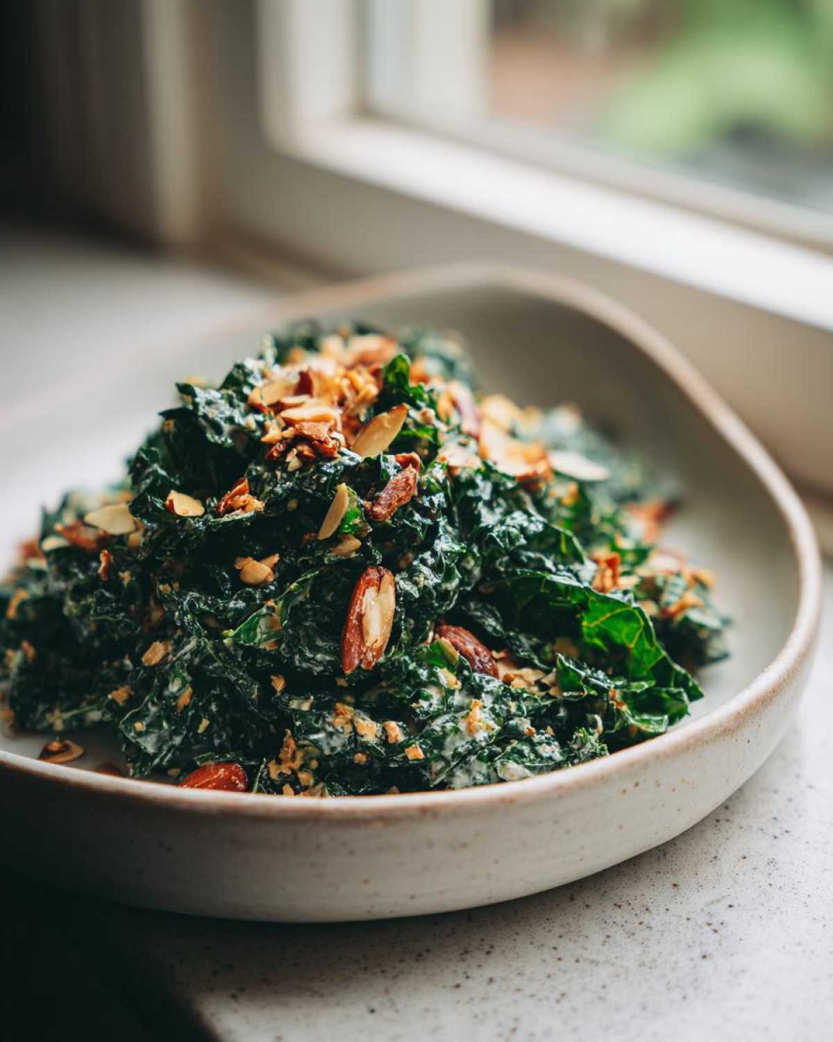 A close-up of the Copycat Kale Crunch Salad, featuring massaged kale tossed in dressing and topped with toasted sliced almonds.