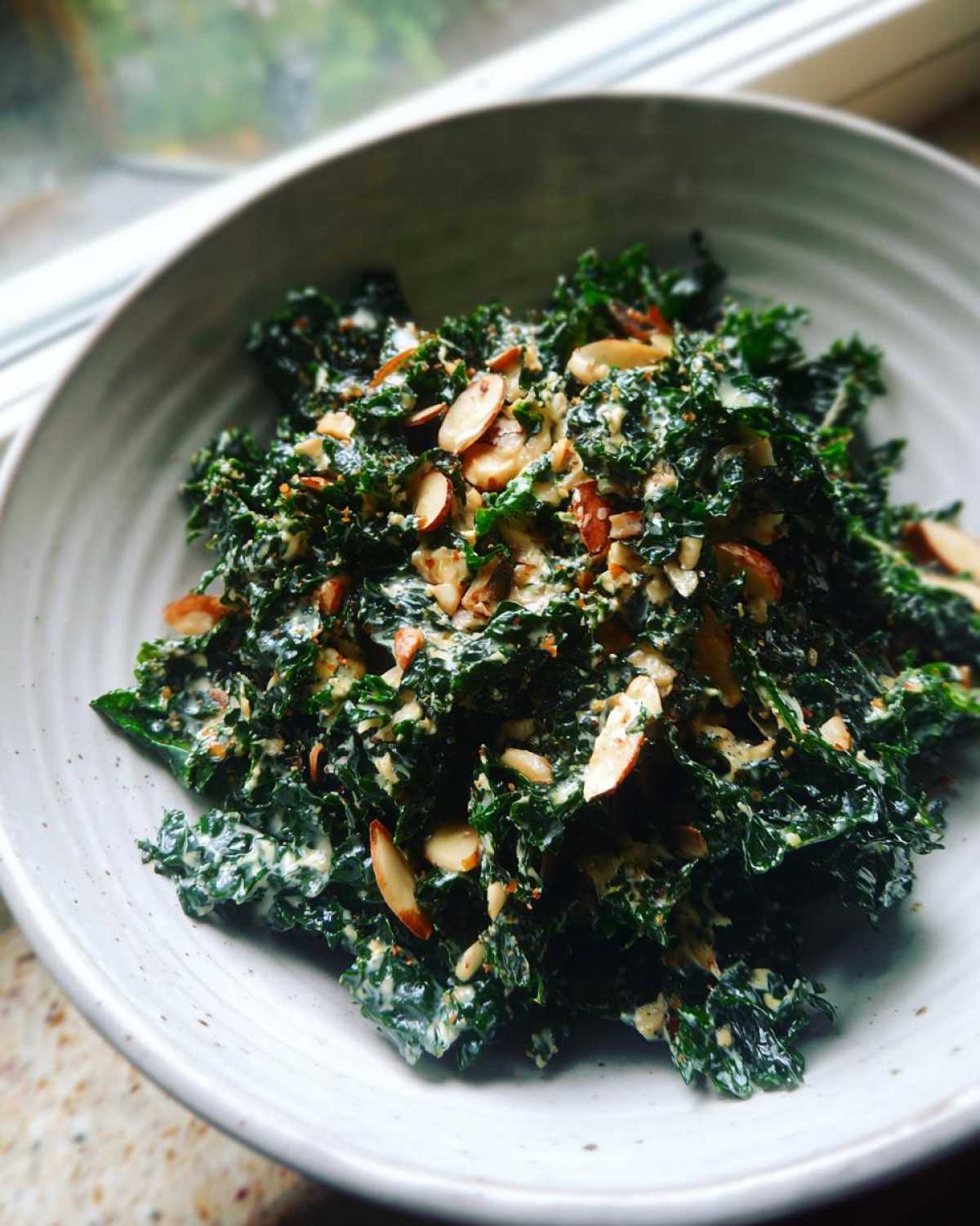 Close-up of Copycat Kale Crunch Salad tossed in a creamy dressing and topped with sliced almonds in a light bowl.