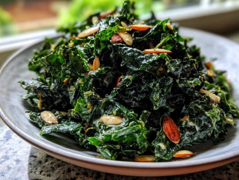 A close-up of a bowl of Copycat Kale Crunch Salad coated in creamy dressing and topped with sliced almonds.