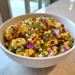 Close-up of a white bowl filled with Copycat Mexican Grill Corn Salsa featuring charred corn kernels, diced red onion, and cilantro.