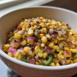 A close-up of vibrant Copycat Mexican Grill Corn Salsa featuring charred corn, red onion, and jalapeño in a white bowl.