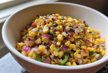 A close-up of vibrant Copycat Mexican Grill Corn Salsa featuring charred corn, red onion, and jalapeño in a white bowl.