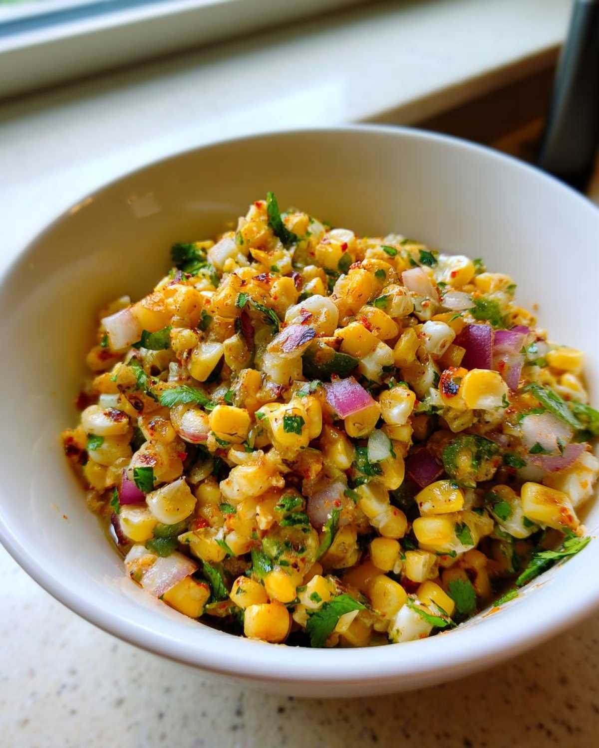 A close-up of a white bowl filled with Copycat Mexican Grill Corn Salsa, featuring charred corn, red onion, and cilantro.