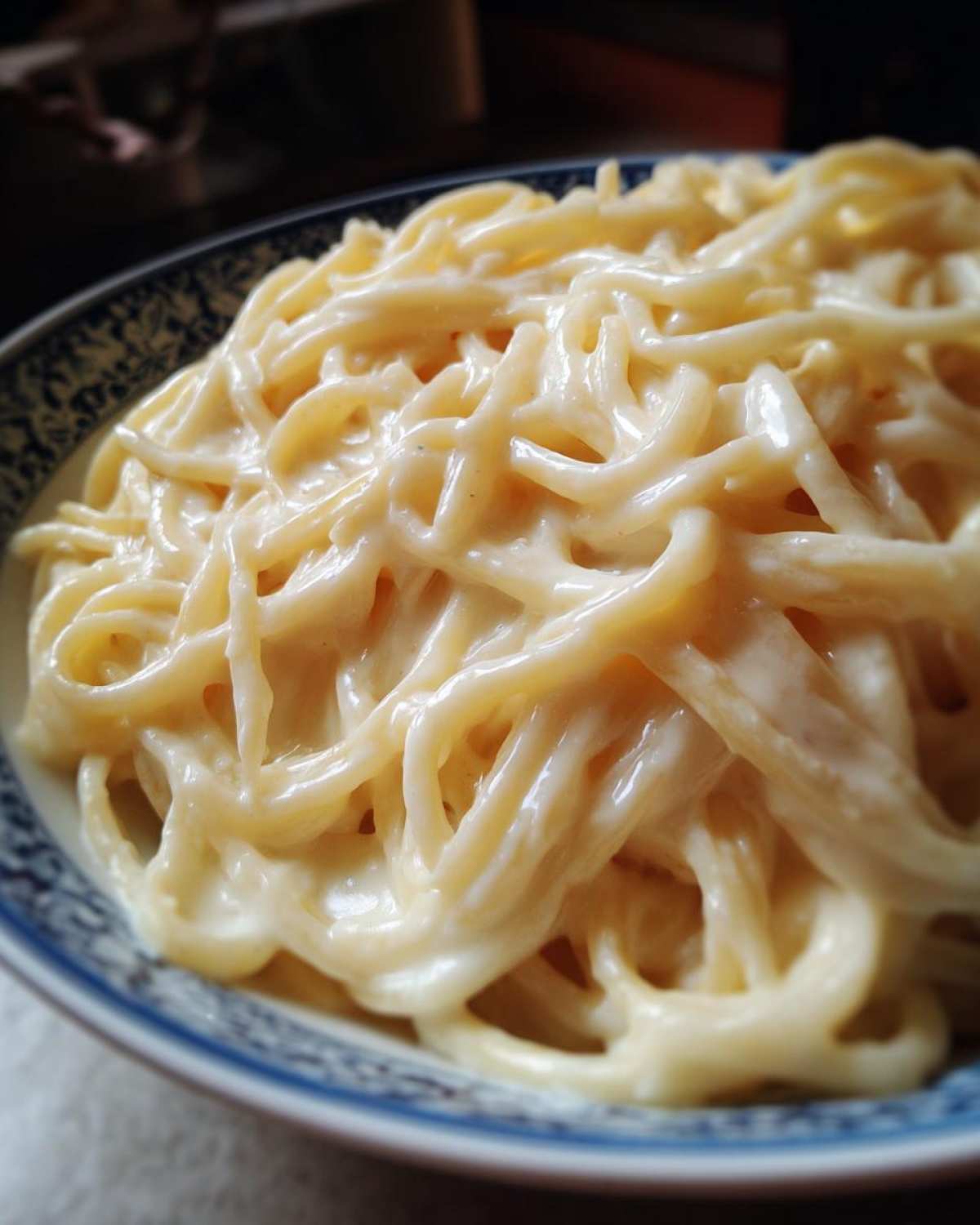 Close-up of spaghetti coated in creamy Easy Cottage Cheese Alfredo Sauce served in a blue and white patterned bowl.