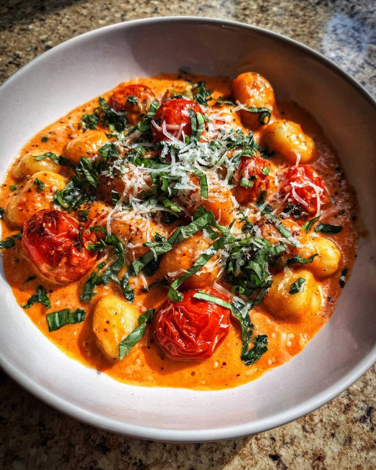 A close-up of Creamy Roasted Garlic Tomato Gnocchi Bake topped with fresh basil and grated Parmesan cheese.