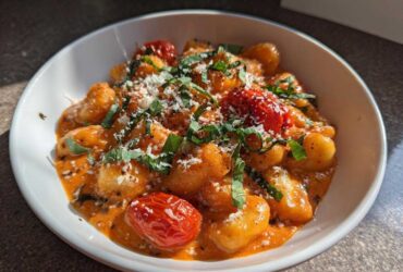 A close-up of the Creamy Roasted Garlic Tomato Gnocchi Bake served in a white bowl, topped with Parmesan and basil.