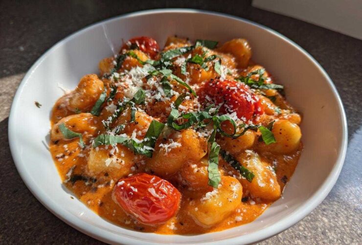 A close-up of the Creamy Roasted Garlic Tomato Gnocchi Bake served in a white bowl, topped with Parmesan and basil.