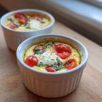 Two servings of Easy 5-Minute Microwave Egg Caprese Cups topped with cherry tomatoes and basil in white ramekins.