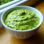 Close-up of a bright green Easy 5-Minute Salsa Verde Yogurt Dip, flecked with chopped herbs, served in a white bowl.