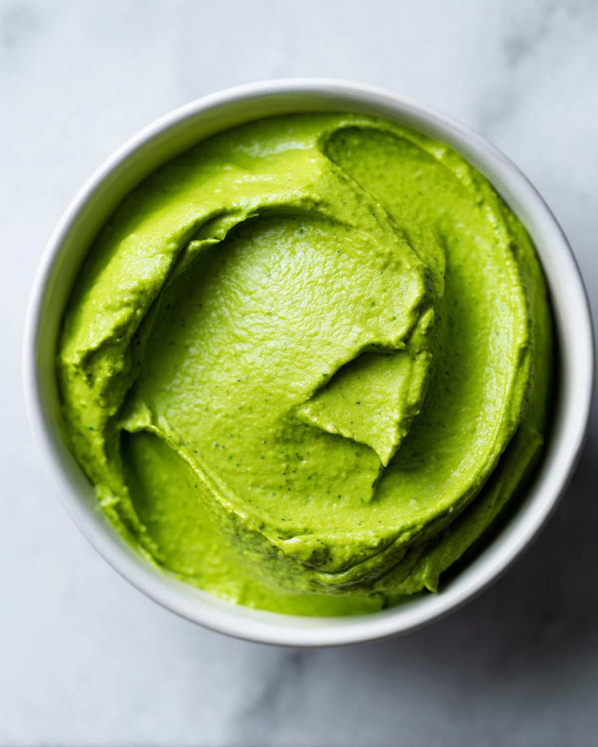 Overhead close-up of vibrant green Easy 5-Minute Salsa Verde Yogurt Dip swirled in a white bowl.