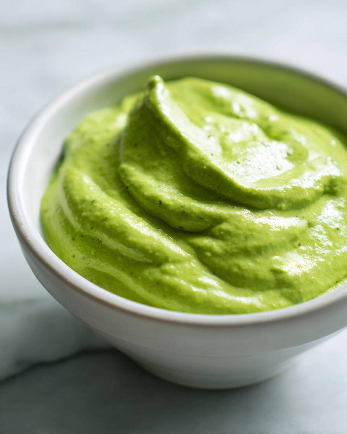 Close-up of vibrant green Easy 5-Minute Salsa Verde Yogurt Dip swirled in a small white bowl.