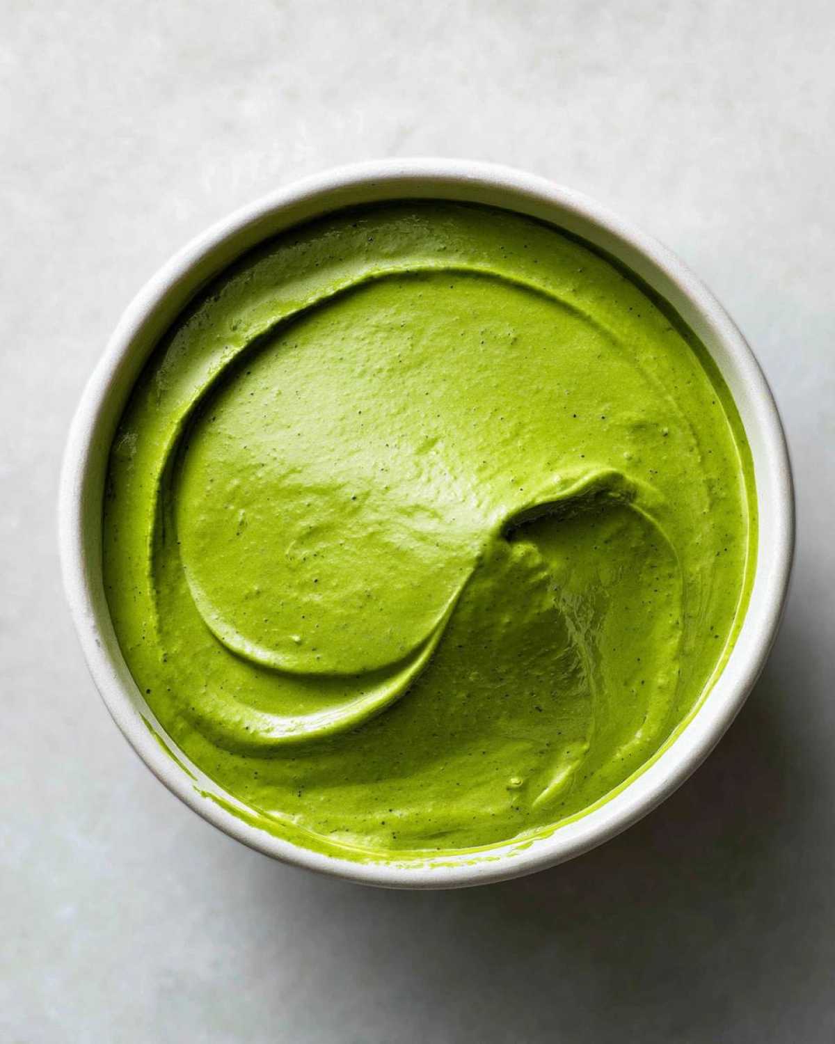Overhead view of a vibrant green Easy 5-Minute Salsa Verde Yogurt Dip swirled in a small white bowl.