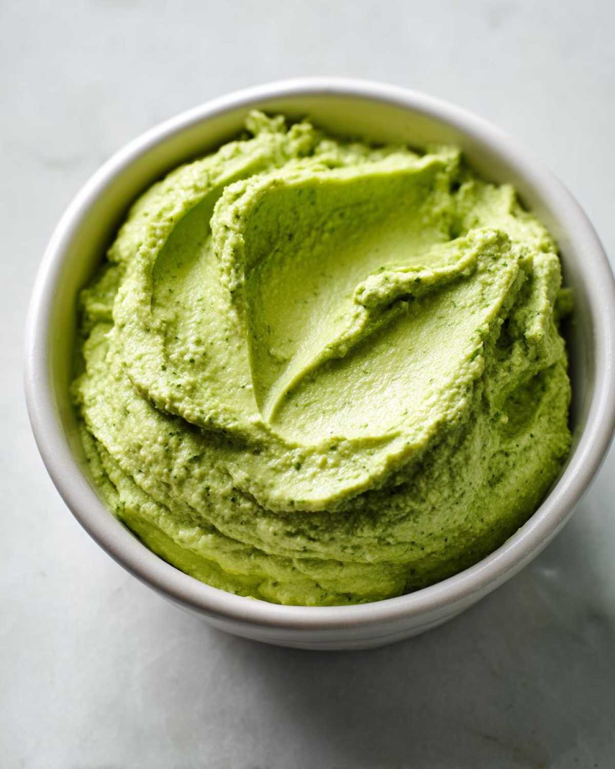Close-up of vibrant green Easy 5-Minute Salsa Verde Yogurt Dip swirled in a small white bowl.