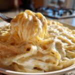 A fork lifting creamy fettuccine coated in Easy Cottage Cheese Alfredo Sauce, seasoned with pepper.