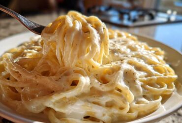 A fork lifting creamy fettuccine coated in Easy Cottage Cheese Alfredo Sauce, seasoned with pepper.