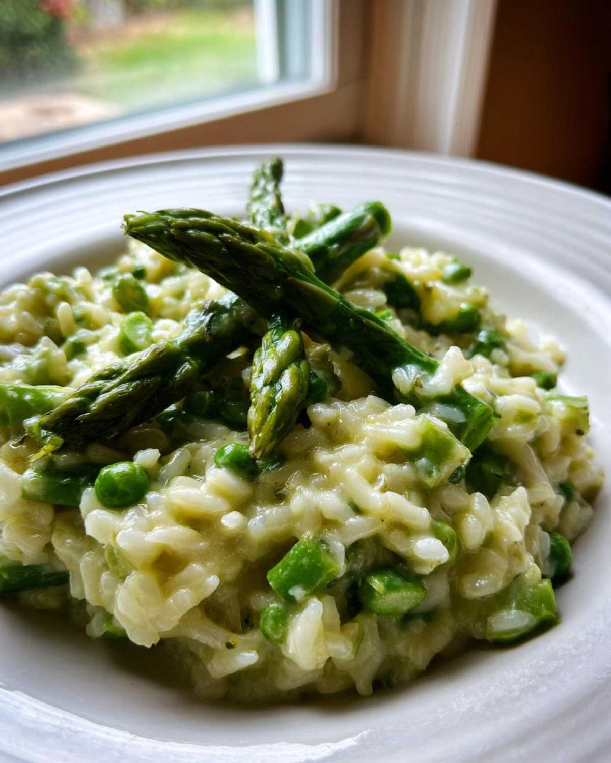 Close-up of Easy Creamy Asparagus Risotto mixed with bright green peas and topped with whole asparagus spears.