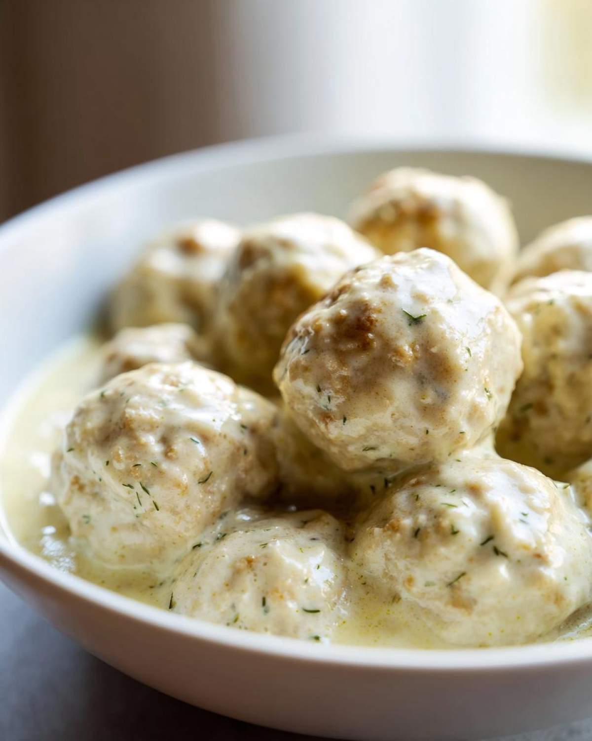 A close-up shot of several Easy Creamy Greek Chicken Meatballs smothered in a rich, light-colored sauce speckled with dill.