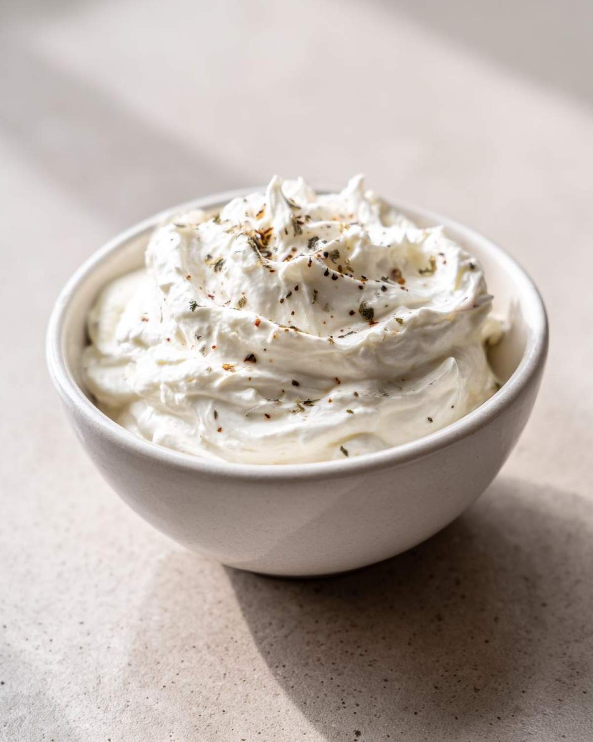 A close-up of thick Easy Greek Yogurt Caesar Dressing, swirled high in a small white bowl and topped with herbs.