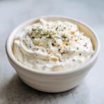 Close-up of thick Easy Greek Yogurt Caesar Dressing topped with grated cheese, pepper, and a sprig of rosemary.