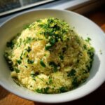A white bowl filled high with fluffy Easy One-Pot Creamy Lemon Herb Couscous, topped generously with fresh parsley and lemon zest.
