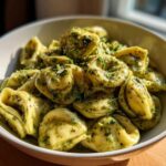 A white bowl filled with Easy One-Pot Creamy Pesto Tortellini, coated in vibrant green pesto sauce.