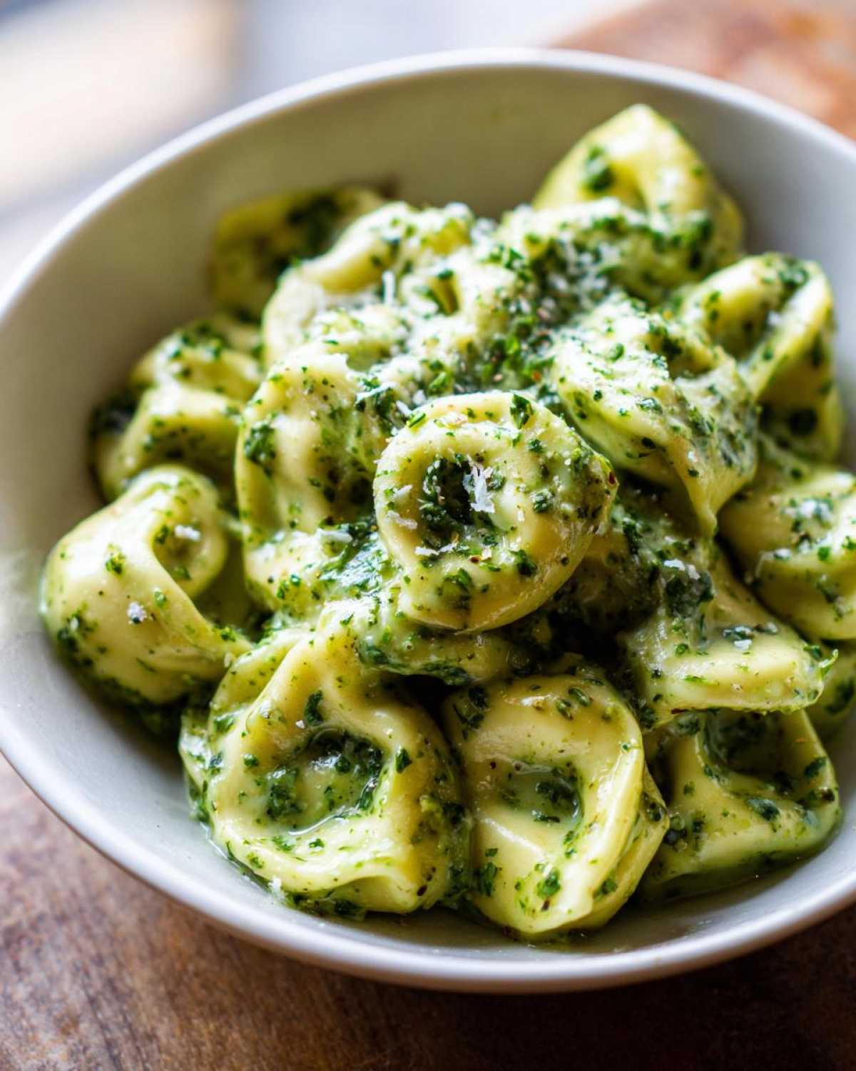 Close-up of Easy One-Pot Creamy Pesto Tortellini coated in vibrant green sauce and topped with grated cheese.