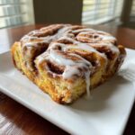 Close-up of a single square serving of the Easy Sheet Pan Cinnamon Roll Bake, drizzled heavily with white icing.