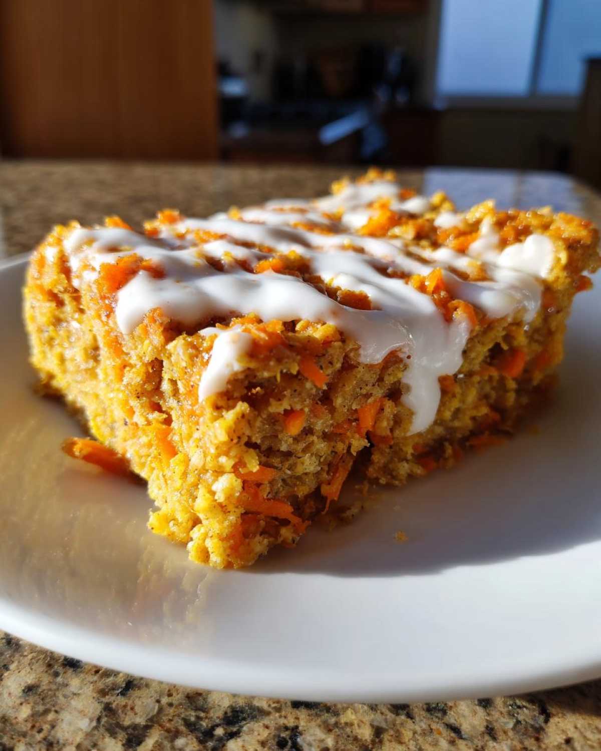 A close-up slice of moist Gluten-Free Carrot Cake Baked Oats topped with white icing drizzle.