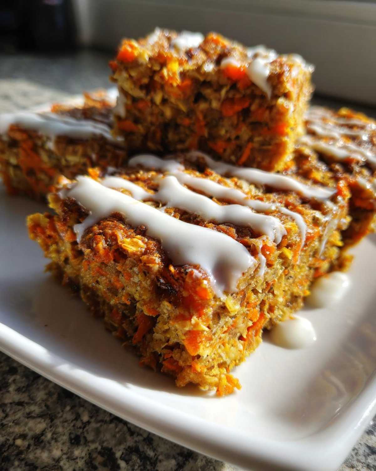 Close-up of square slices of Gluten-Free Carrot Cake Baked Oats drizzled with white icing on a white plate.