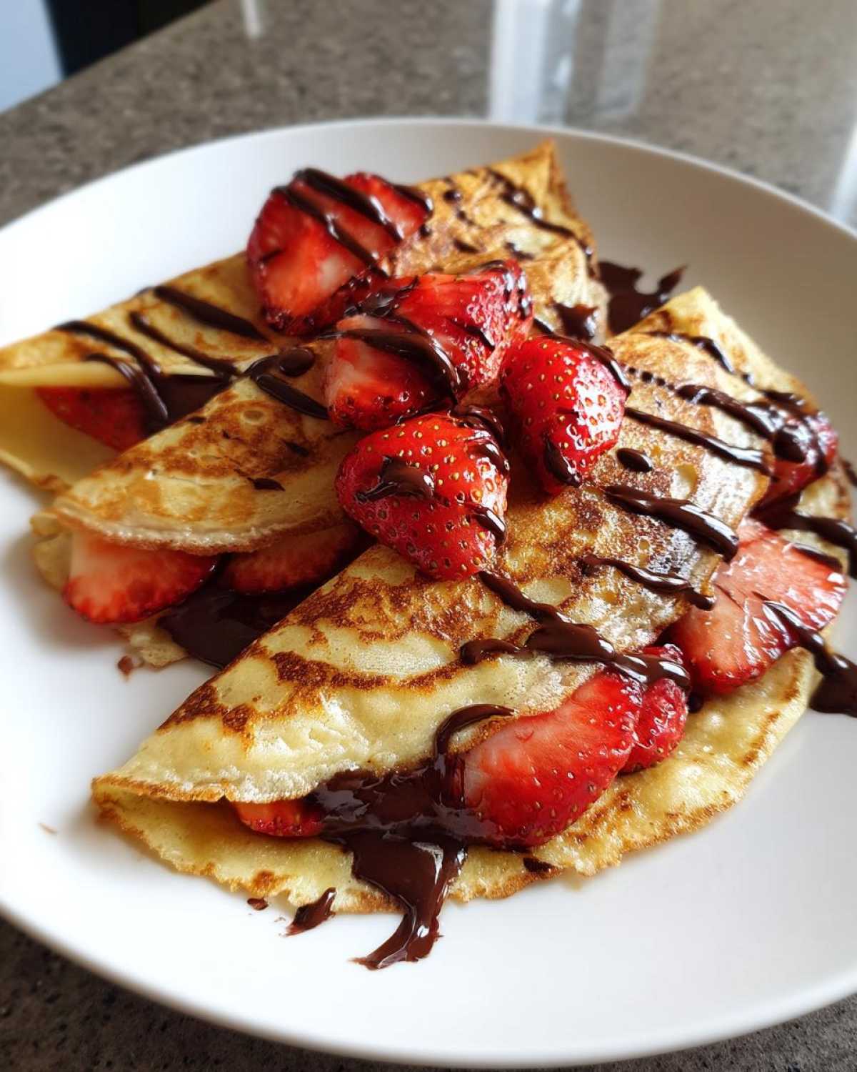 Close-up of folded Gluten-Free Chocolate Strawberry Crepes topped with fresh strawberries and drizzled with chocolate sauce.