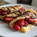 Close-up of three folded Gluten-Free Chocolate Strawberry Crepes drizzled with chocolate sauce on a white plate.