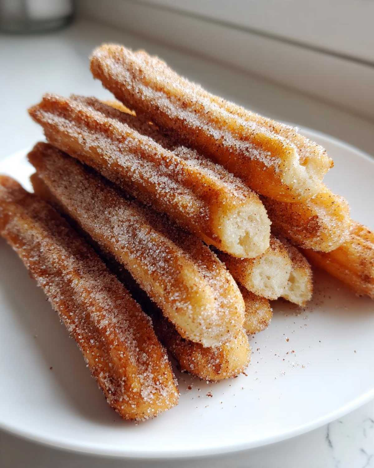 A stack of crispy Gluten-Free Cinnamon Sugar Waffle Sticks heavily coated in cinnamon sugar, resting on a white plate.